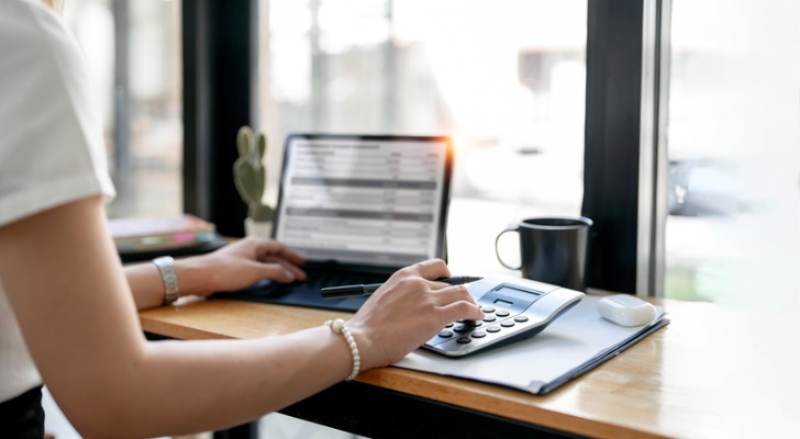 A close-up of a woman working on a tablet and calculator. 