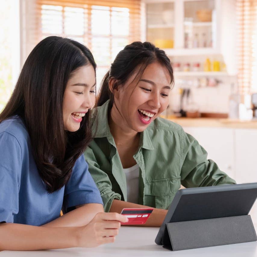 Asian couple using tablet and credit card to shop online on kitchen table at home.